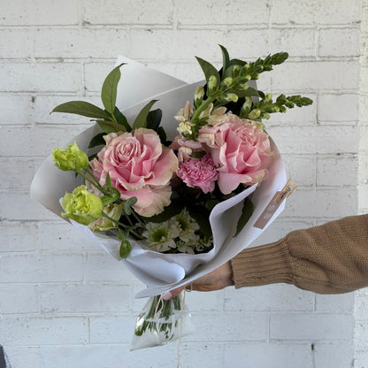 Bouquet of pink and green flowers held against a white brick wall.