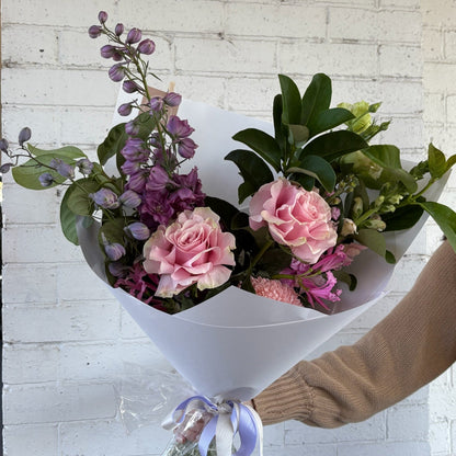 Bouquet of pink and purple flowers held by a person against a white brick wall.