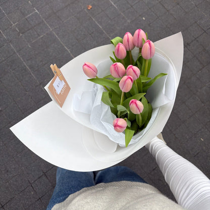 Bouquet of pink tulips held by a person on a gray pavement.